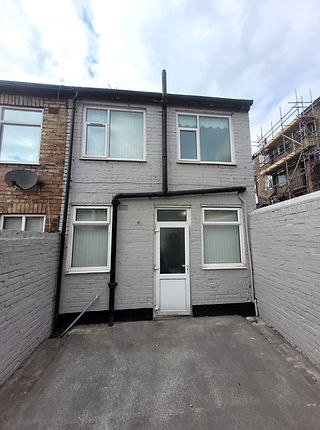 Rear exterior of a terraced house with freshly painted light grey brickwork, white uPVC windows and door, and a clean concrete patio area.