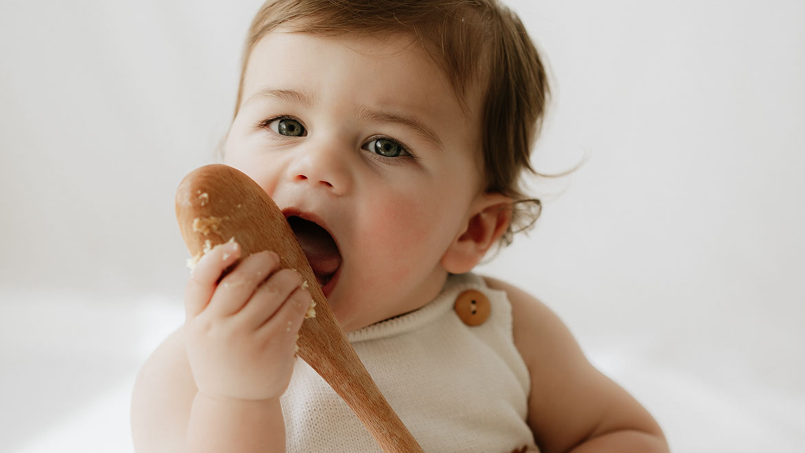 one year old licking spoon during cakesmash photoshoot