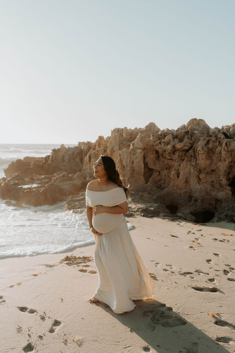 expectant mum wearing a white dress on the beach