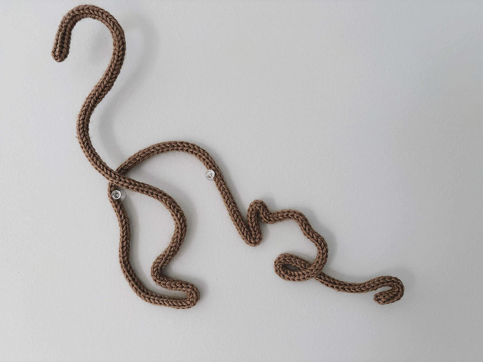 a knitted decor wall hanging of a cat stretching, in the colour latte.
