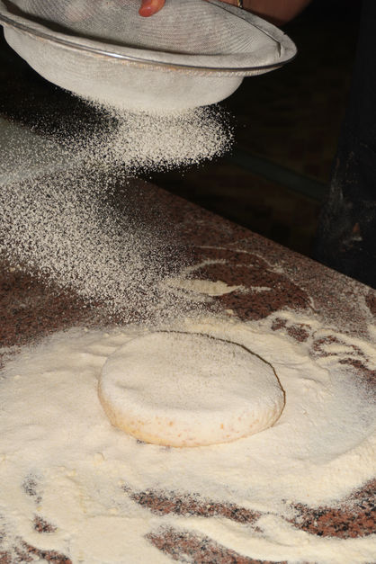 Flour being sprinkled on dough on a wooden surface.