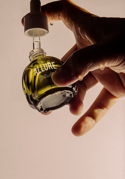 Hand holding a small perfume bottle labeled "ALLURE".