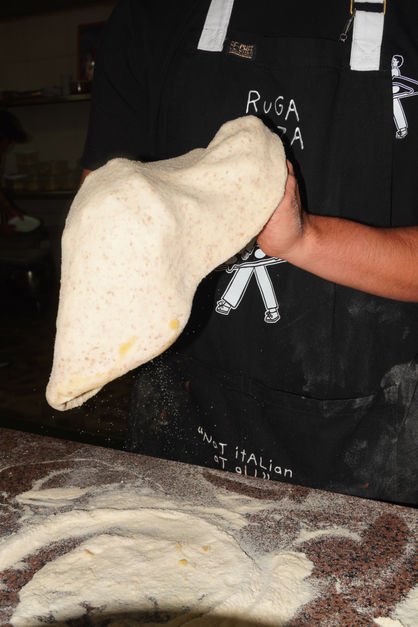 Person holding pizza dough in a kitchen.