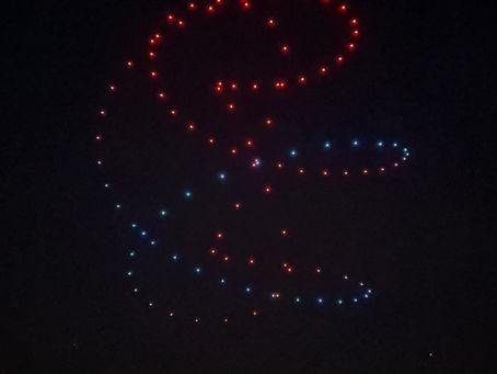 drones forming a swirling ribbon/spiral (red/blue) over a city horizon — grand opening event ideas