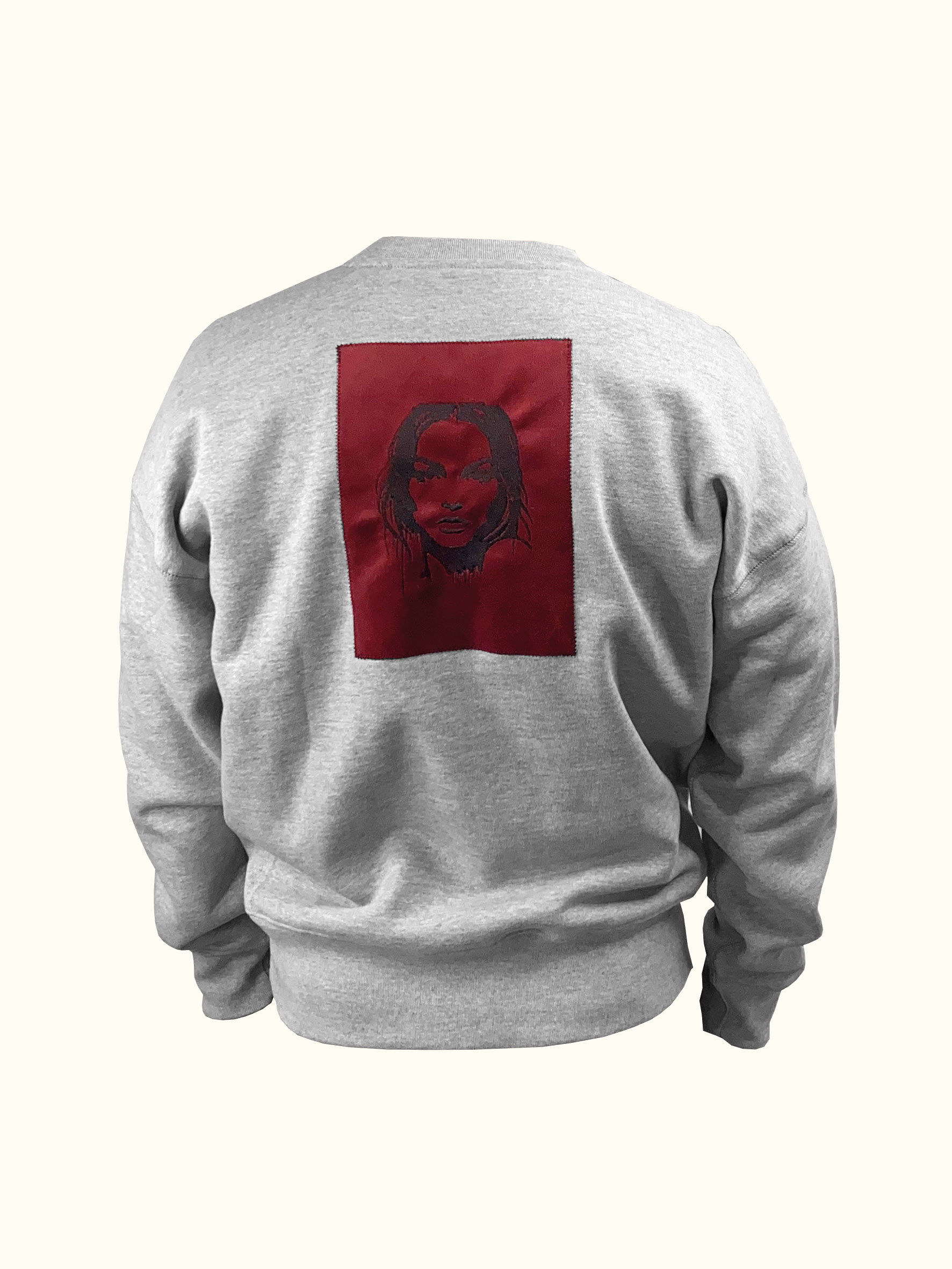 Grauer Sweater mit aufgenähtem roten Patch auf dem Rücken. Patch ist in schwarz bestickt mit dem Gesicht einer Frau.