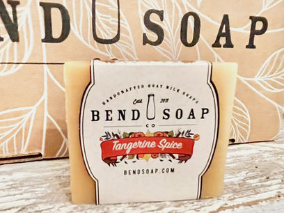 Bar of Bend Soap Co. Tangerine Spice Goat Milk Soap on a white weathered wood table with a Bend Soap Co. gift box backdrop.