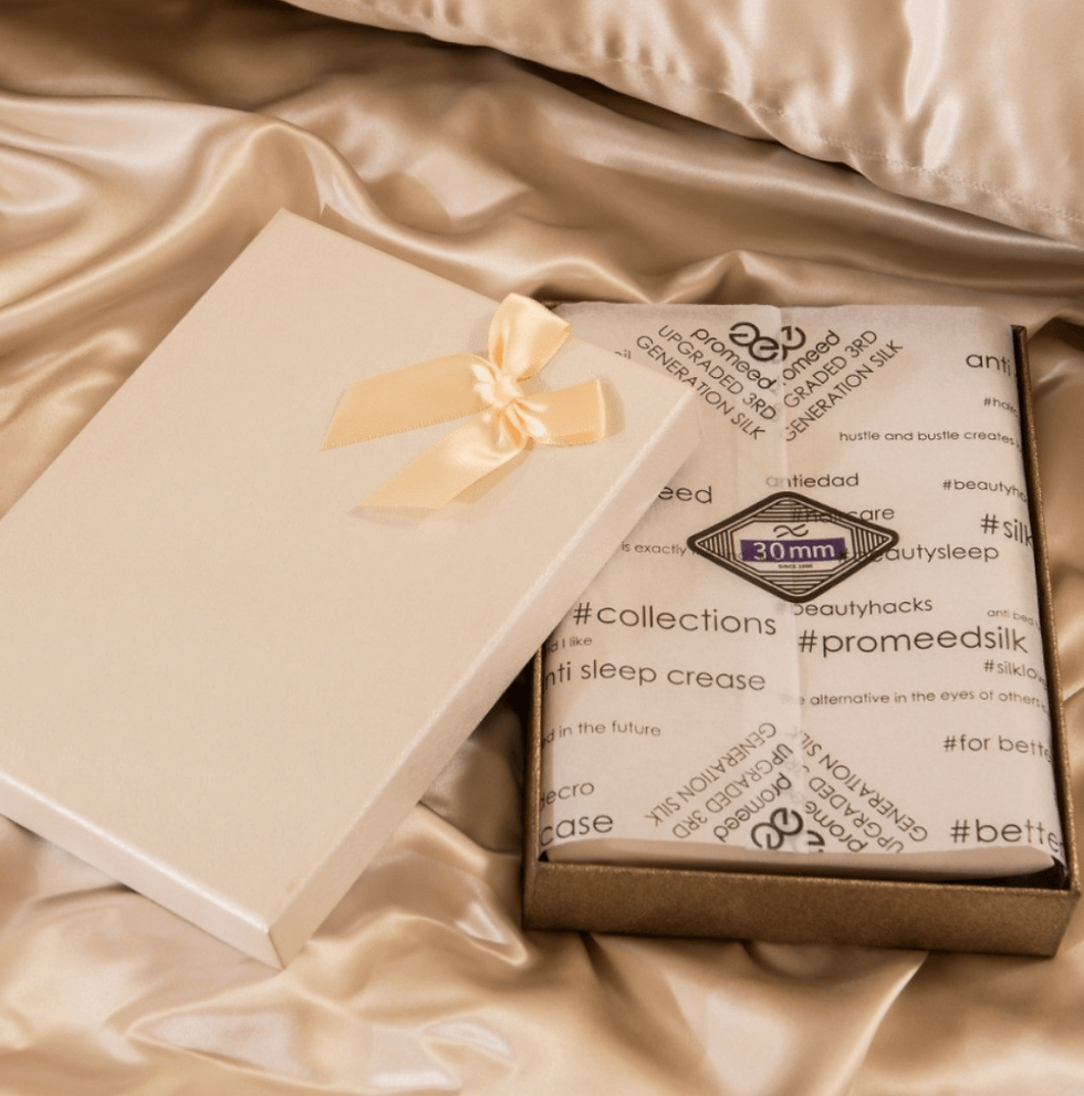 Thumbnail: Promeed Organic Mulberry Silk Pillowcase Champagne. In box with logo tissue paper on silk sheets.