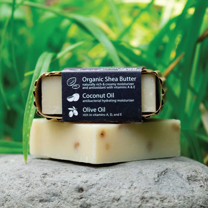 Hemlock Park Bar Soap in packaging laying on its side stacked on unpacked soap bar with tropical foliage backdrop