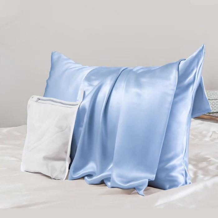 Thumbnail: Promeed Organic Mulberry Silk Pillowcase Baby Blue. On a pillow sitting on a bed with laundry bag.