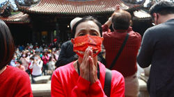 A lady wearing a red face mask praying with her hands together, and a Taiwanese Taoist temple and cr