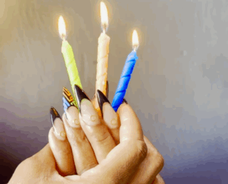 A hand holding lit candles with nail polish colors representing BAYCAT's brand colors—blue, green, and orange—creating a festive and celebratory atmosphere.