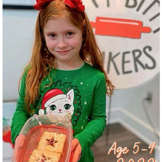 Girl in green holiday shirt holding pastries in a clear container, smiling indoors. Background has "Itty Bitty Bakers." Text: "Age 5-9, 2022."