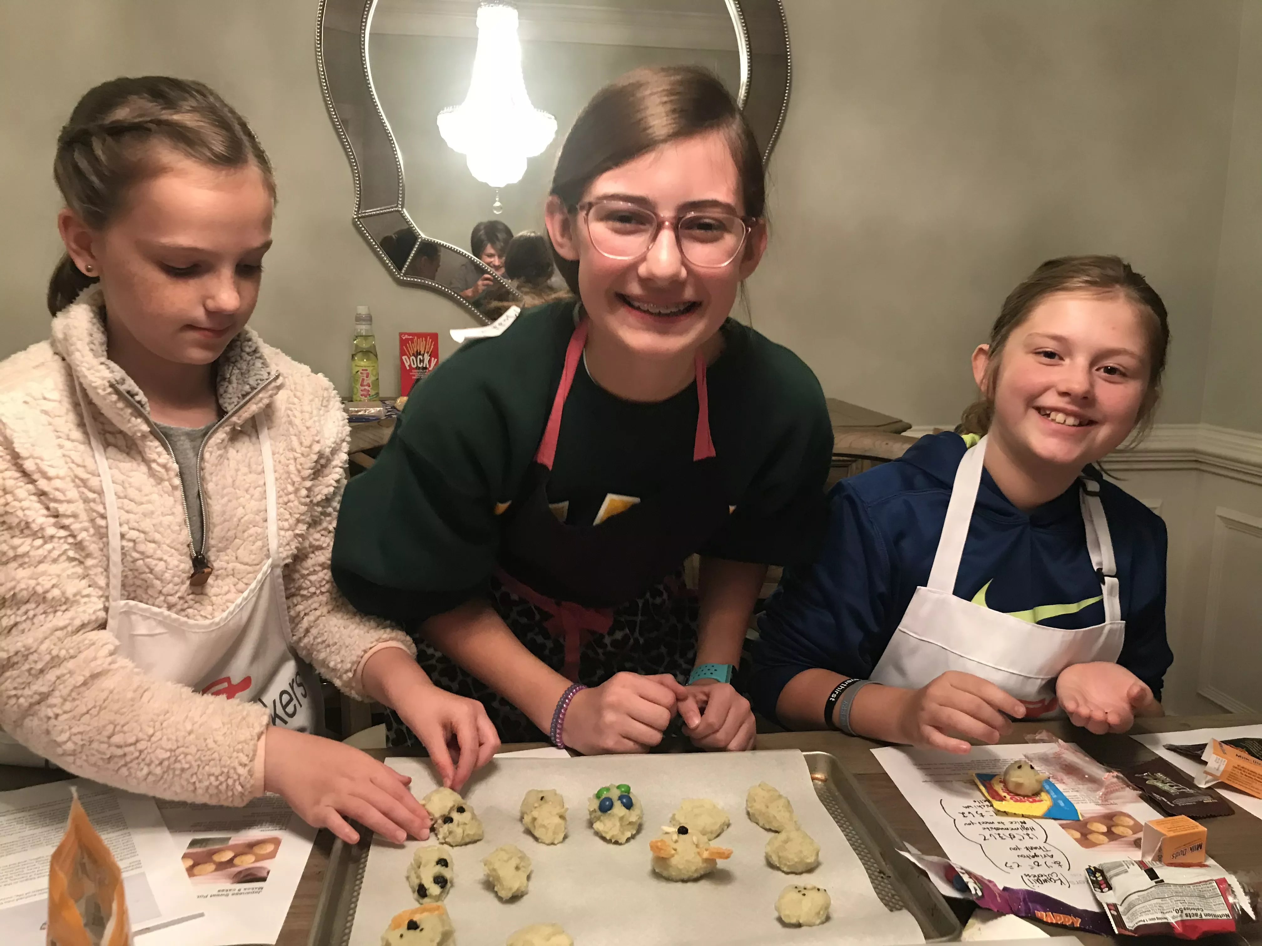 three teen girls stand looking at a baking sheet