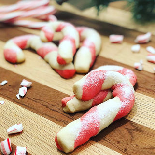 Candy cane-shaped cookies with red and white swirl on a wooden surface, surrounded by candy pieces and greenery, creating a festive mood.