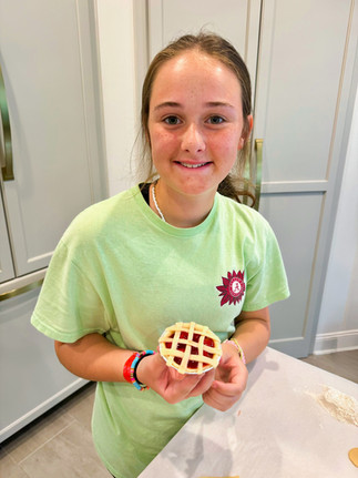 teen girl stands at kitchen counter holding completed mini cherry pie with lattice crust