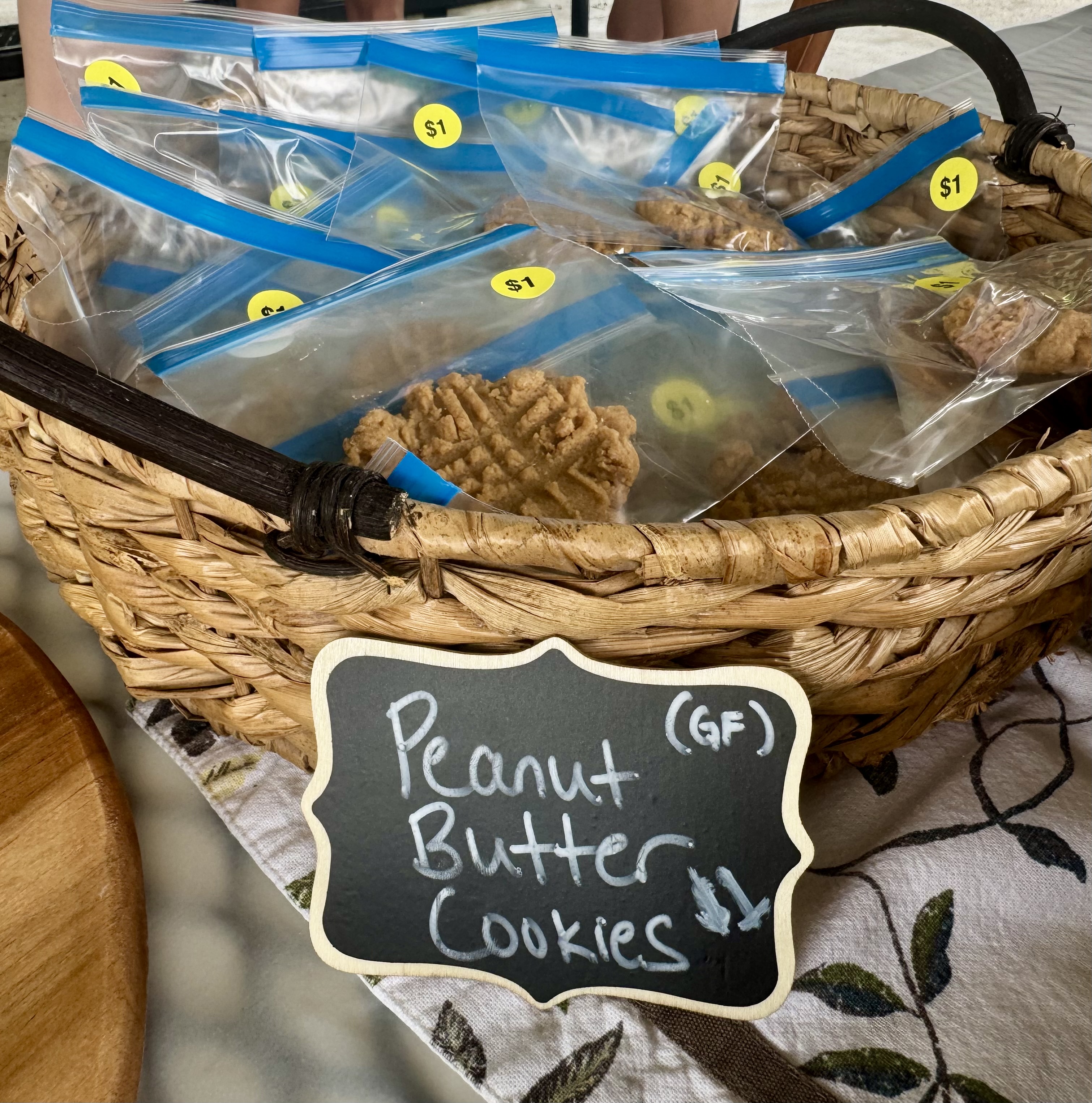 Basket of zip-top bags with peanut butter cookies, $1 stickers, and GF chalk sign on a table.