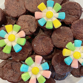 Brownie bites topped with colorful candy flowers in yellow, blue, green, and pink, arranged on a white plate.