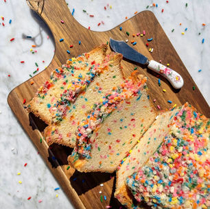 Eye-level view of a loaf of freshly baked rainbow sprinkle bread on a wooden cutting board