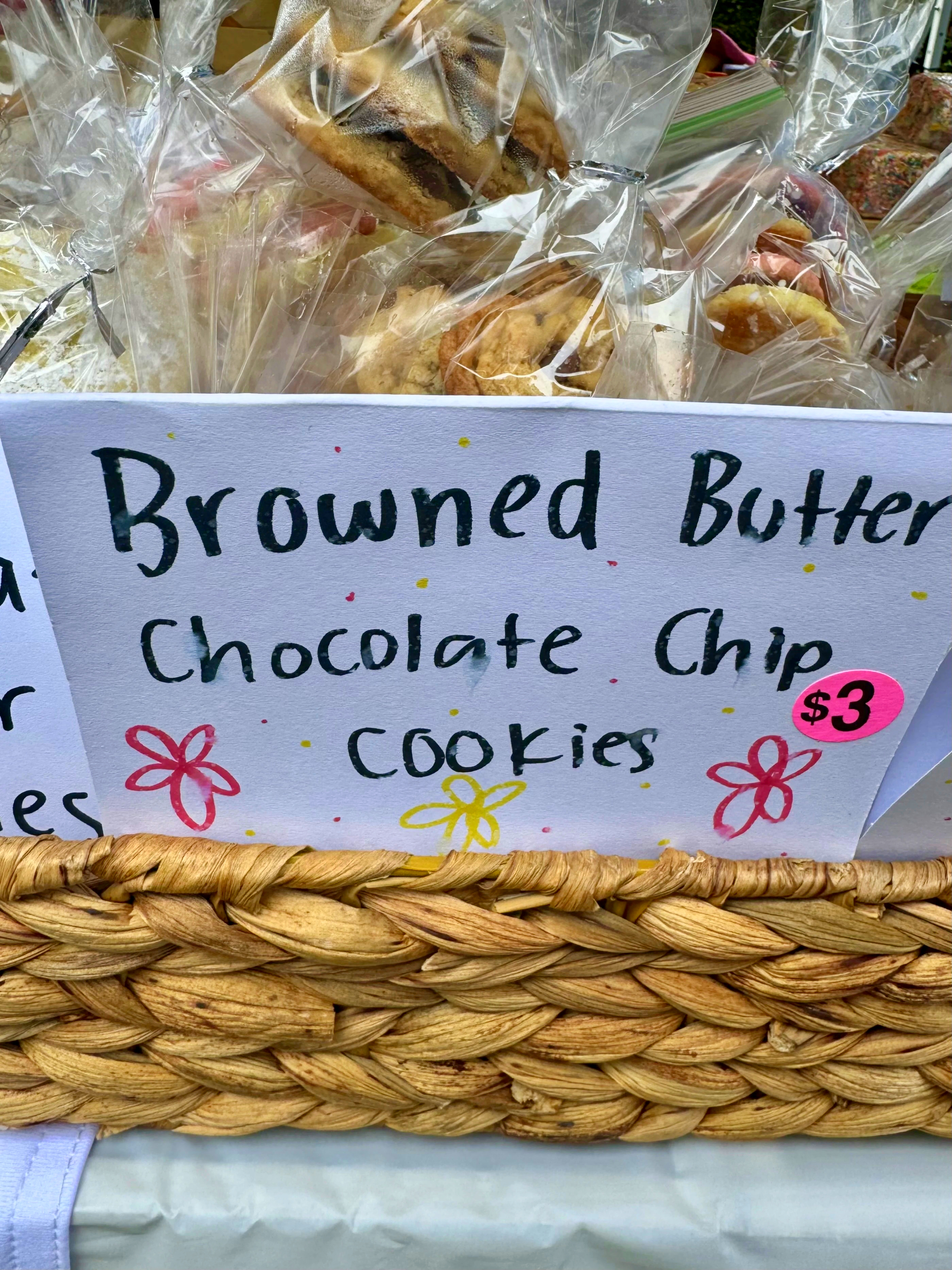 Bagged browned butter chocolate chip cookies in a woven basket with a hand-lettered $3 sign.