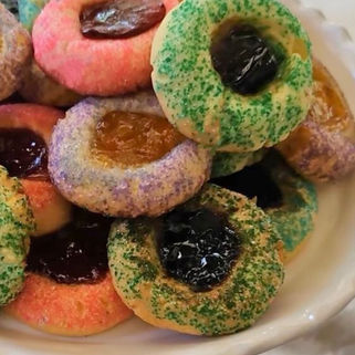 Plate of colorful thumbprint cookies with jam centers and green sprinkles, piled on a white dish in a bright kitchen