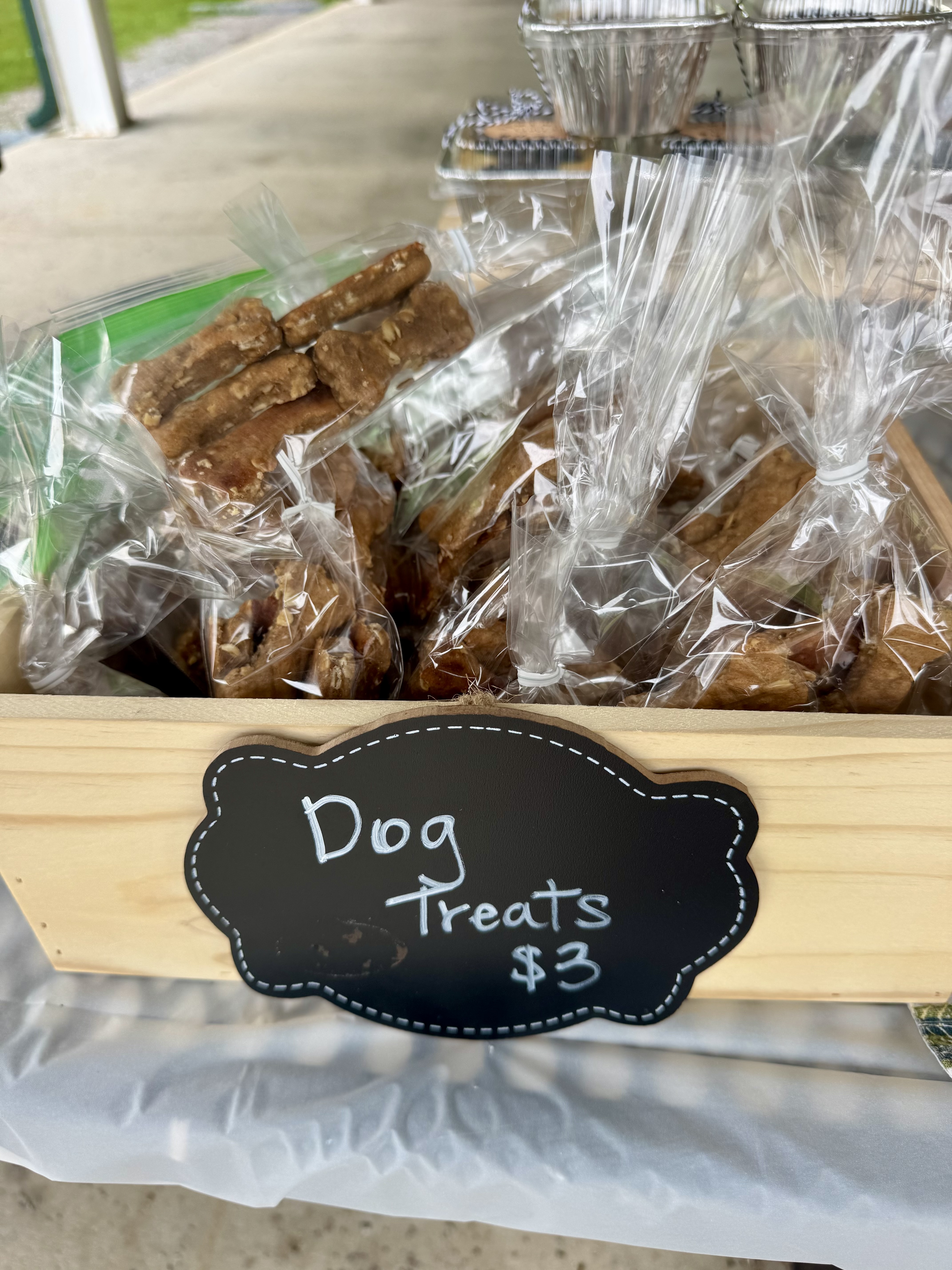 Clear plastic bags of homemade dog treats on a wooden table, with a chalkboard sign reading Dog Treats $3.