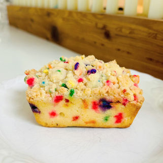 Colorful sprinkle cake slice with crumb topping on a white plate. Wooden background, bright and cheerful setting.