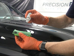 Gloved detailer applies ceramic coating to a green applicator at Precision Auto Detailing workshop.