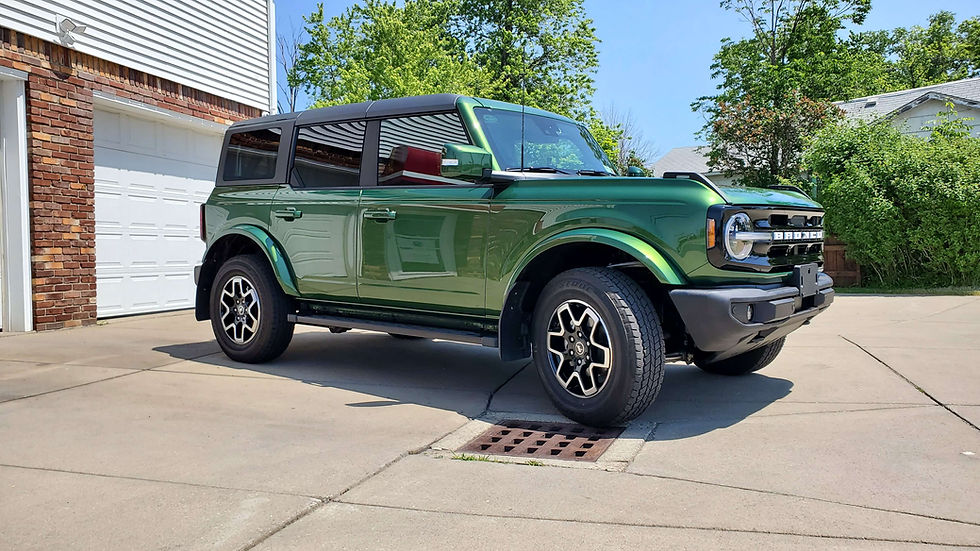 Green Ford Bronco after ceramic coating service with black roof parked on driveway, brick and white garage in background. Sunny day with trees and blue sky in suburban setting.