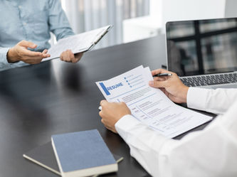Vista ravvicinata di un colloquio di lavoro su una scrivania nera. In primo piano, le mani di un recruiter in camicia bianca che tengono una penna e un curriculum vitae stampato