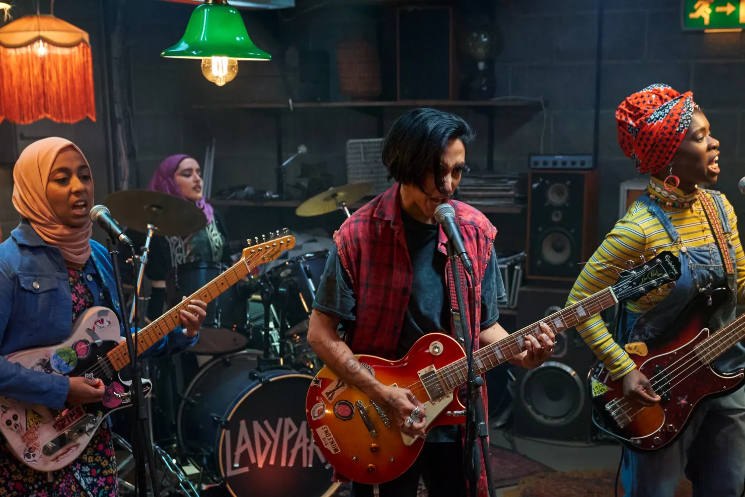 Band from show "lady parts" rehearsing punk rock song wearing hijabs, headscarves and grunge clothing.