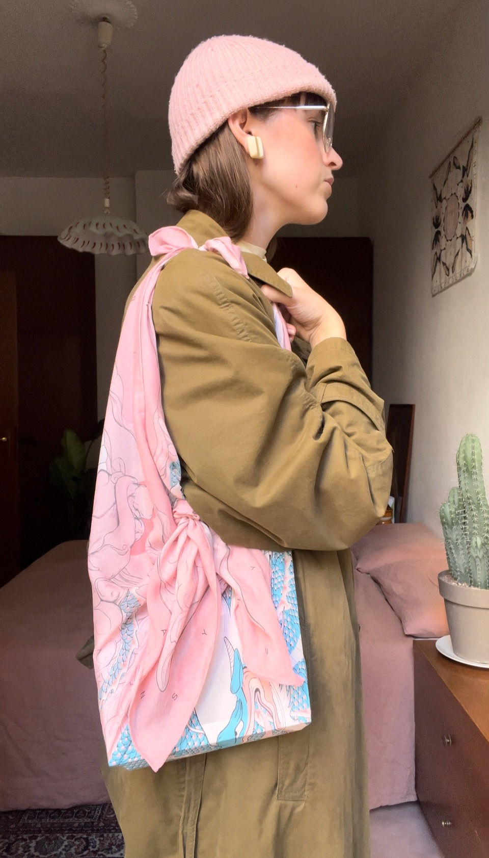 Still frame from "how to tie a silk scarf into a bag" tutorial. Woman wears square scarf as a tote.