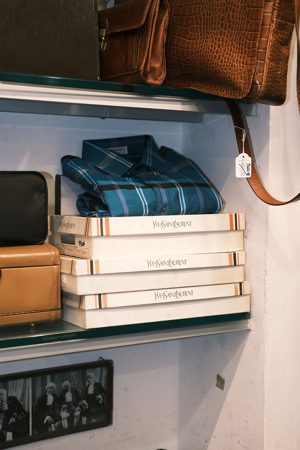 Bookshelves filled with vintage Italian leather handbags, blue button up shirt, and designer fashion boxes.