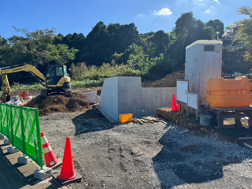 造成工事現場全景。重機が入り、コンクリート擁壁や仮設トイレなどが設置された高低差のある土地の工事風景。