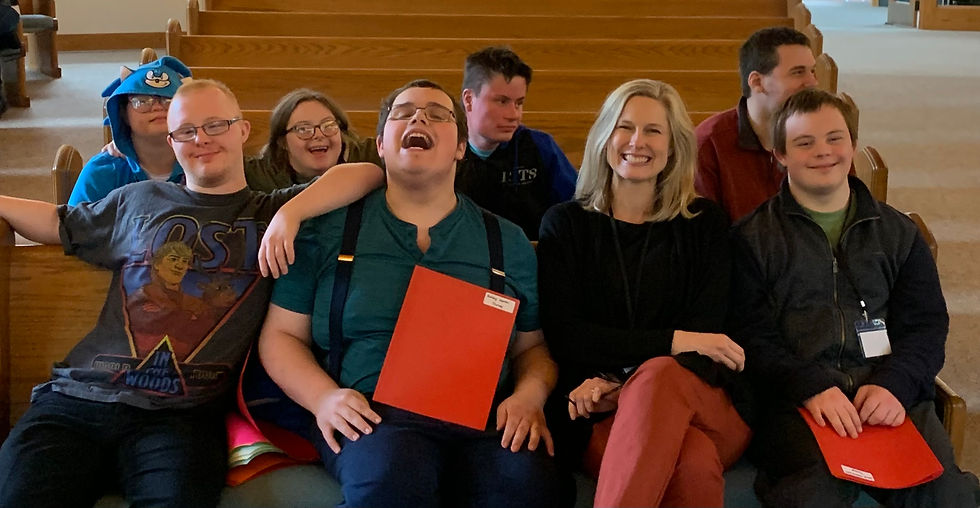 Students and Teaching Artist Erin Epp sitting together in pews at their rehearsal location, all smiling at the camera.