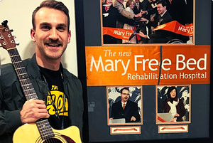 Young white man (John Nowak) holds up an acoustic guitar and smiles next to a poster with the title "Mary Free Bed Rehabilitation Hospital"