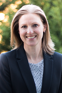 Smiling woman with long brown hair and a black top against a gray background. Mood is calm and positive.