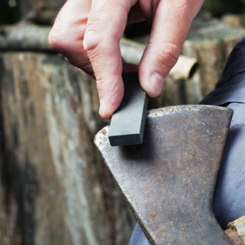 a hand holding a flint is sharpening an axe 