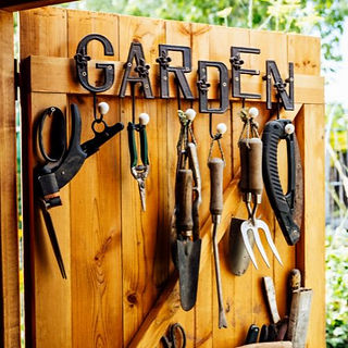 wooden door to a shed with garden tools hanging from it and the word "garden" spelled out in antique letters