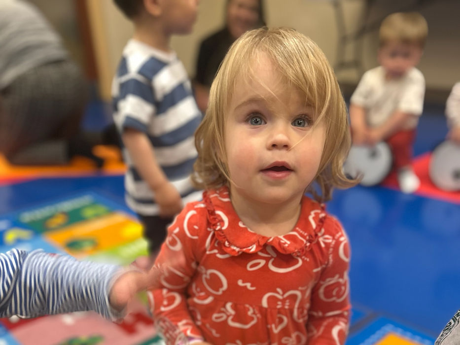 Young child playing a drum during music class with other children