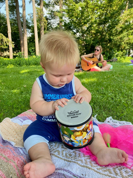 Toddler plays drum at outdoor music class in Brookline