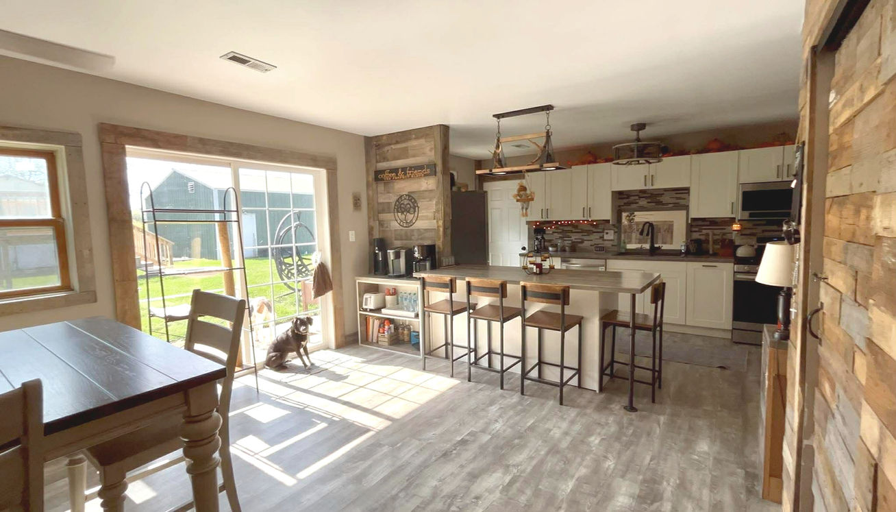 Warm, rustic, modern kitchen remodel with a custom tile backsplash, white cabinets and grey wood countertops. White and gray kitchen island with dark wood stools and a sliding glass door done by Precision Roofing And Remodeling