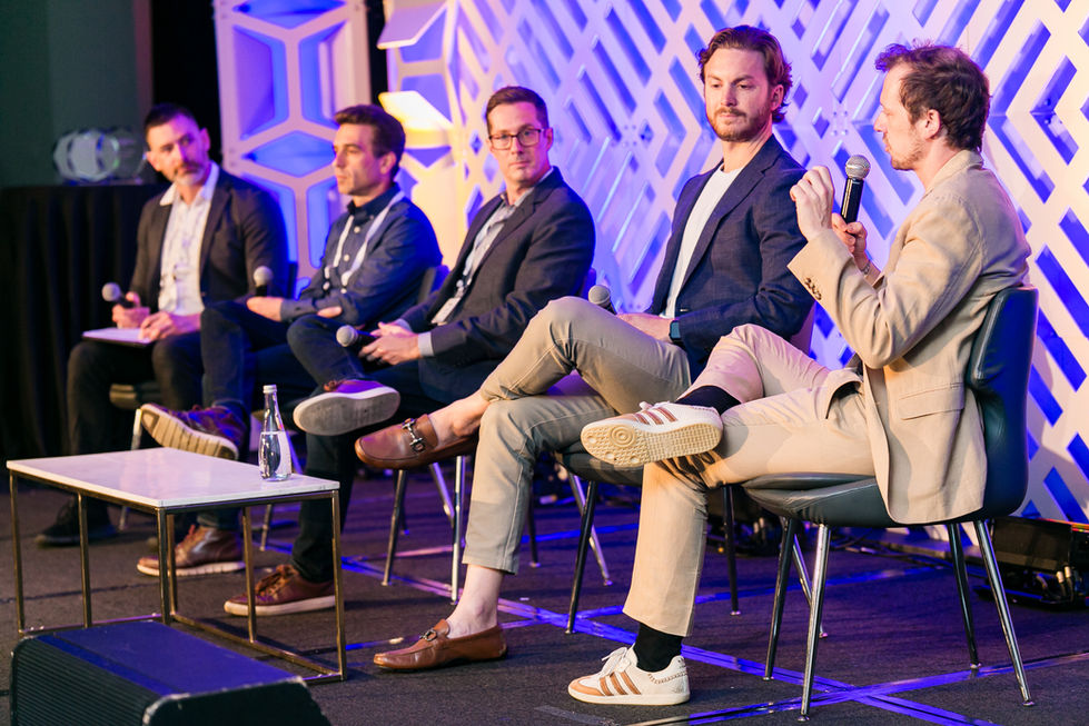 a group of men are sitting in chairs with their legs crossed and one man is holding a microphone