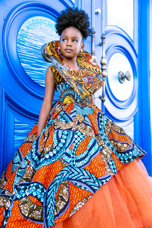 a little girl in a colorful dress stands in front of a blue door
