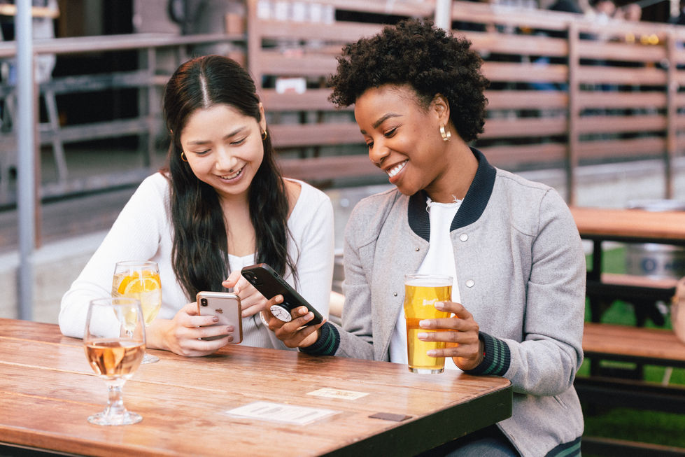 two women sit at a table looking at their phones