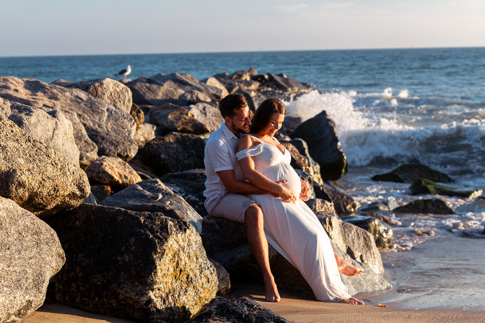 a man and a pregnant woman sit on rocks near the ocean