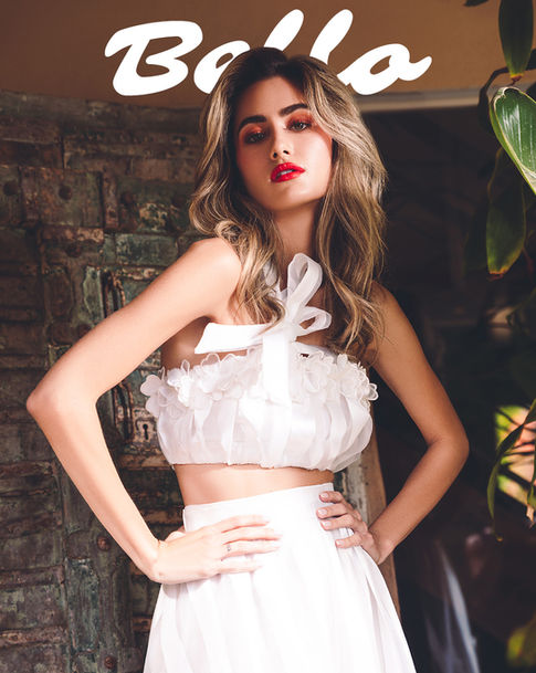 a woman wearing a white crop top and a white skirt