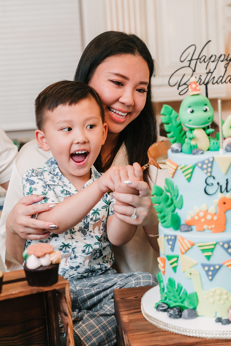 Woman and child cutting a dinosaur birthday cake.