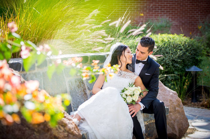 a bride and groom are sitting on a bench in front of a fountain