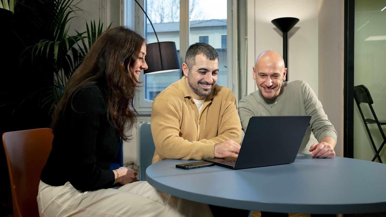Three people working in front of a laptop while smiling