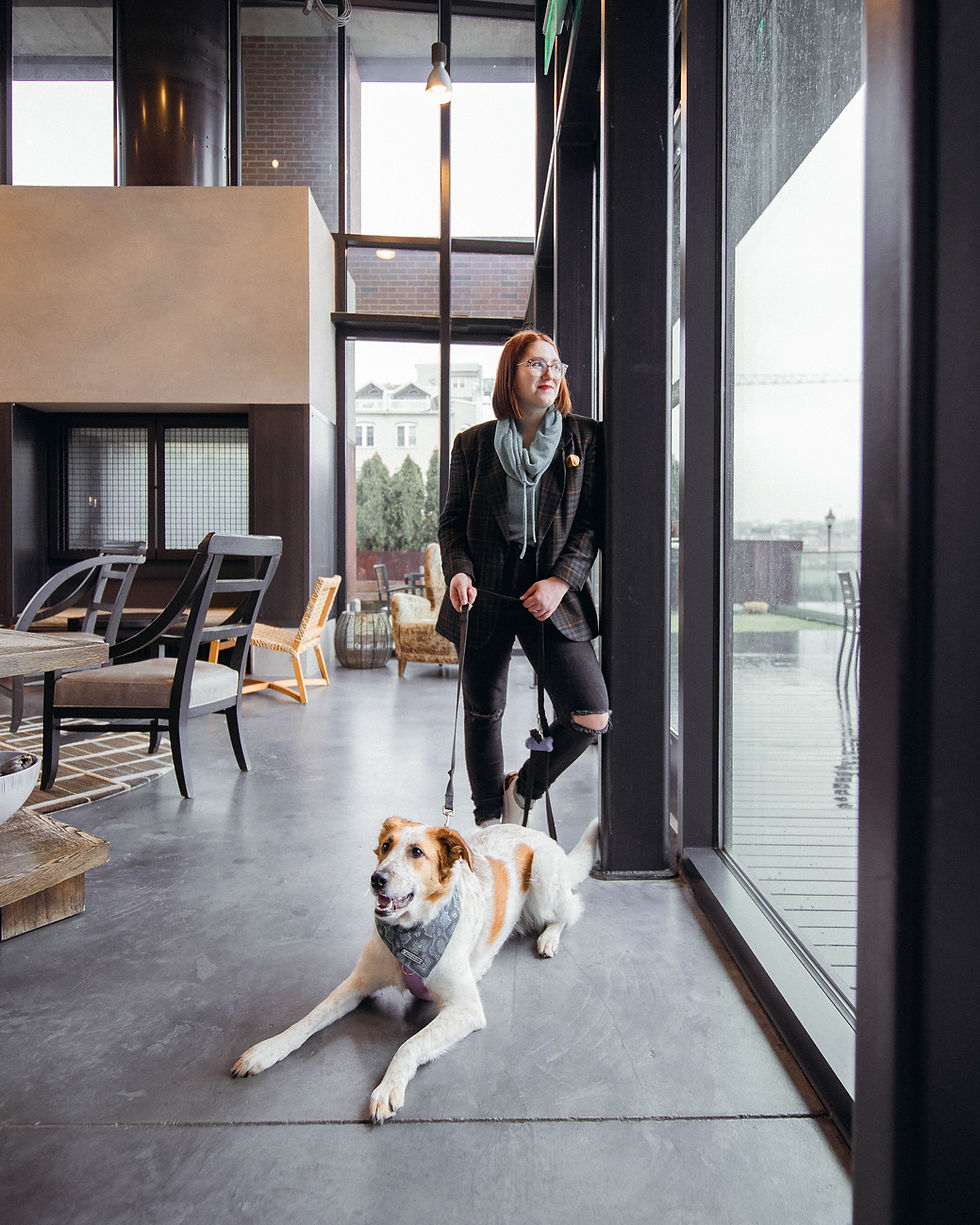 Taylor wearing a jeans, a teal sweatshirt, and plaid blazer as she stands with a dog in Union Wharf's waterfront community space.